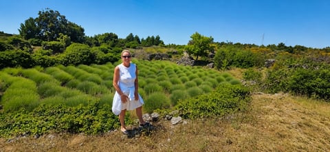 Woman in white dress standing in green hills with lavender fields under blue sky