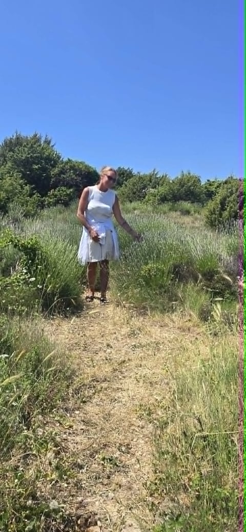 Woman in white dress standing on a dirt path through a wildflower field on a sunny day